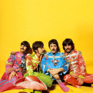 Ringo Starr, John Lennon, Paul McCartney and George Harrison in Sergeant Pepper Lonely Hearts Club Band closing sitting in a studio with a yellow backdrop.